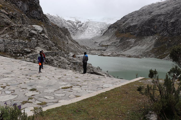 people standing on a dam overlooking a glacial lake