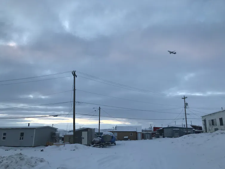 A town in a snowy landscape with a plane flying overhead.