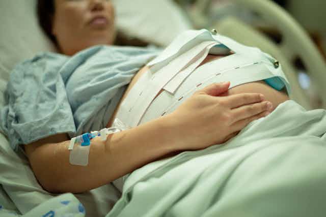 Pregnant woman lays in hospital bed hooked up to fetal heartrate monitor.
