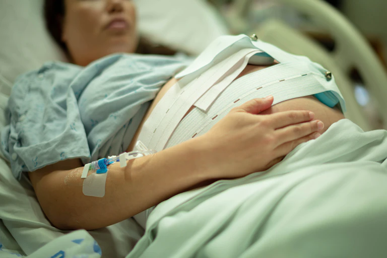 Pregnant woman lays in hospital bed hooked up to fetal heartrate monitor.