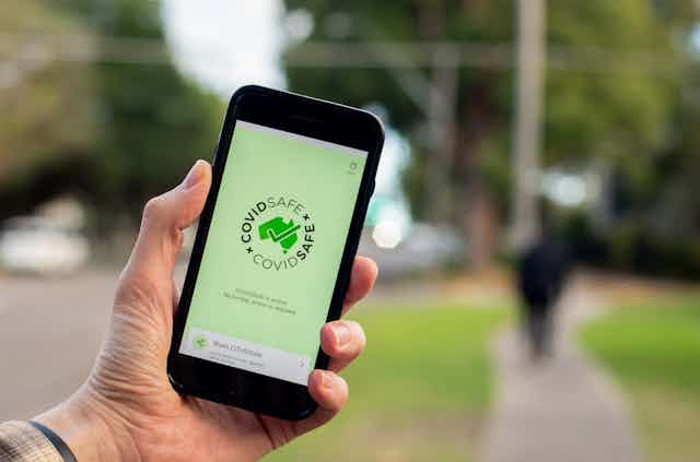 A person holds up a phone displaying the COVIDSafe app.