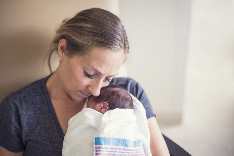 New mother in hospital holds her baby on her chest and closes her eyes.