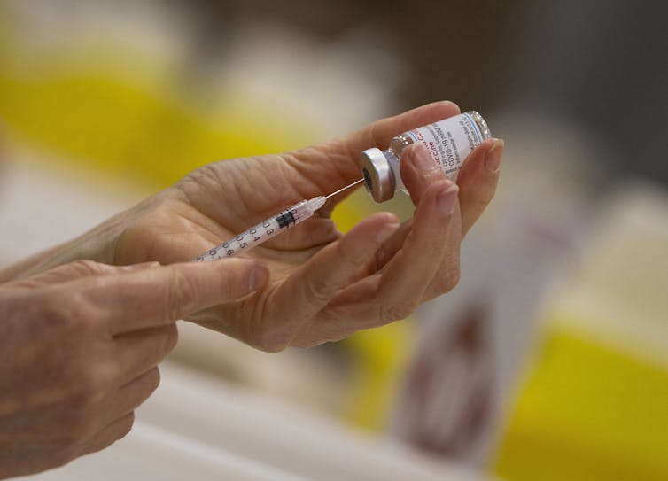 Pharmacist filling a syringe from a vial of on of the COVID-19 vaccines