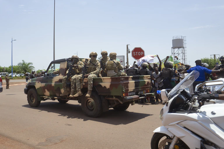 Armed soldiers on the back of a truck driving along a street.