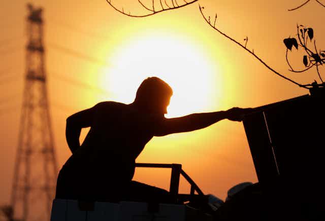 A silhouette of a man loading goods onto a truck at sunset.