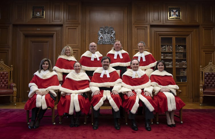 Nine judges in red and white robes pose for a photo.