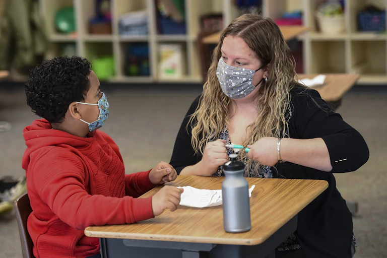 Teacher works with fourth-grade student at school desk