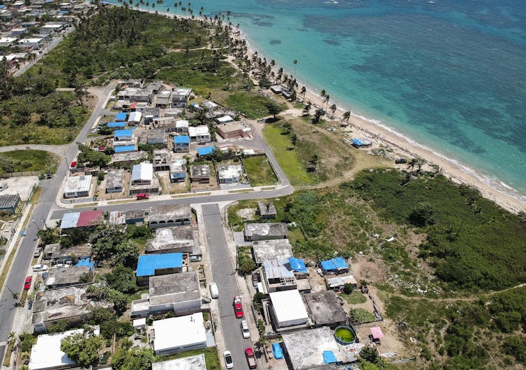 Aerial photo of a seaside neighbourhood with several blue tarps on the roofs of buildings