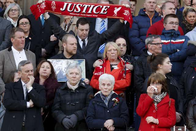 Relatives of the Hillsborough victims gather together in 2016. One is holding a photo of a man who died and another is holding up a red scarf reading 'justice'.