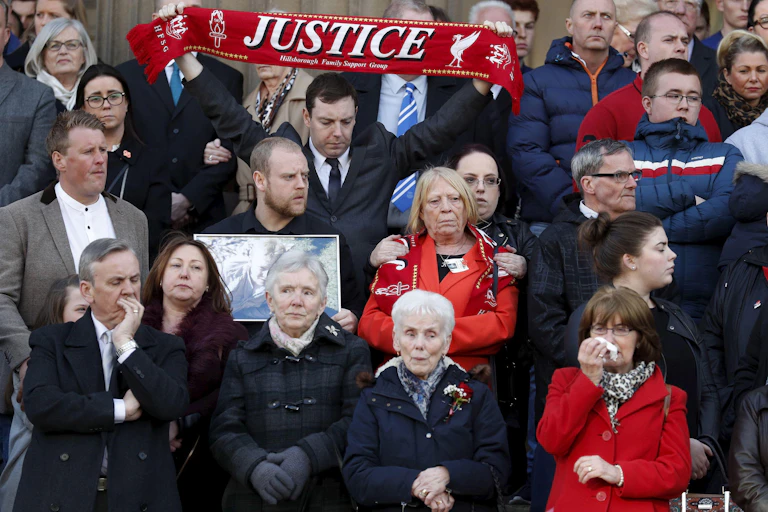 Relatives of the Hillsborough victims gather together in 2016. One is holding a photo of a man who died and another is holding up a red scarf reading 'justice'.