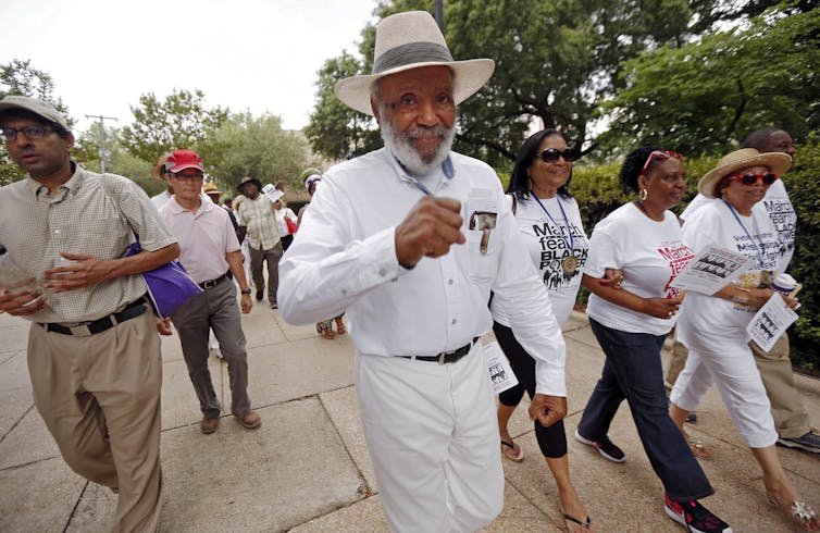 James Meredith, dressed in all white and wearing a straw hat, walks surrounded by others in a 50th anniversary march commemorating his earlier march for voting rights.