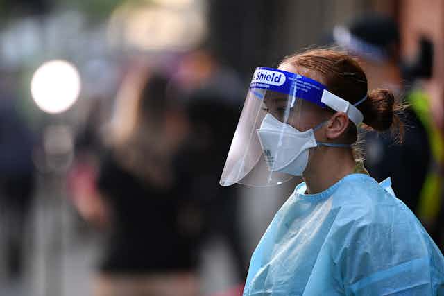 Hotel quarantine worker in PPE stands on the street.