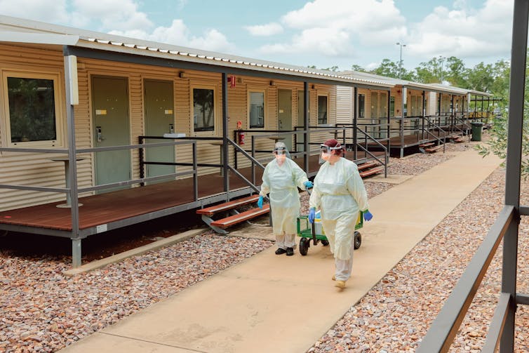 Two workers in PPE walk through the Howard Springs facility.