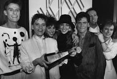 A black and white photo of people in the 1980s including a woman in a white suit and short hair holding a Juno statue.
