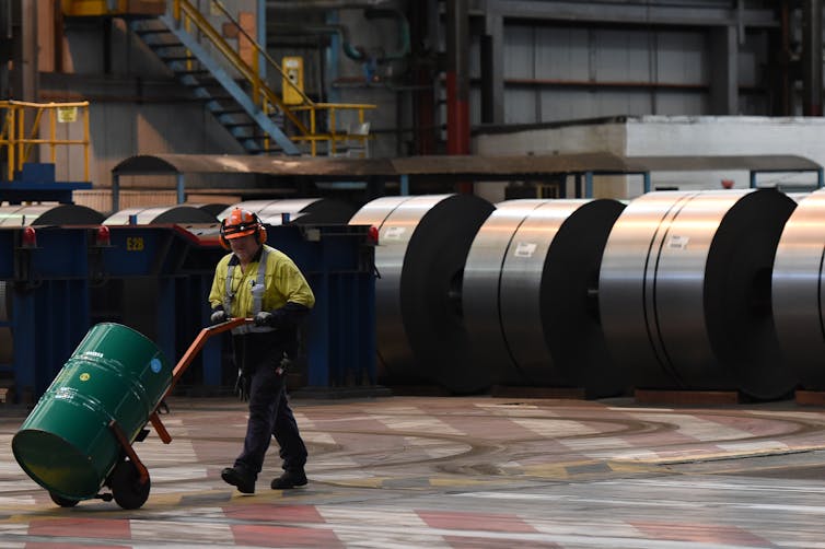 workers walk past rolls of finished steel