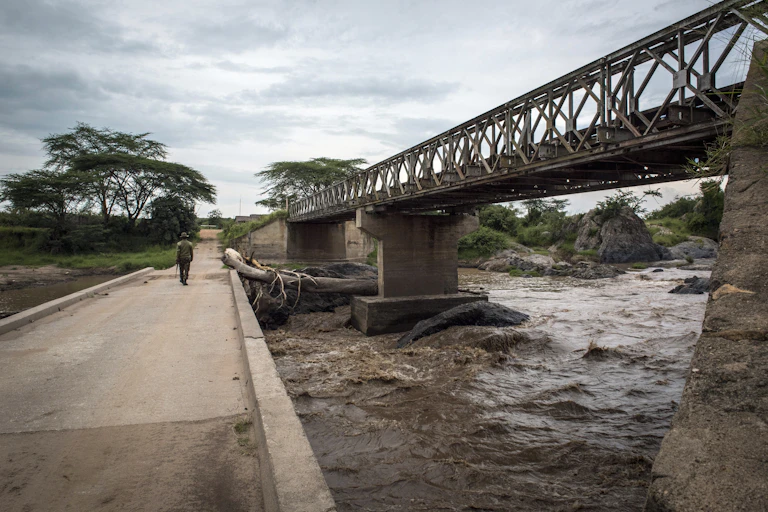 A man walks on a concrete road bridge over a river, next to a higher steel railway bridge