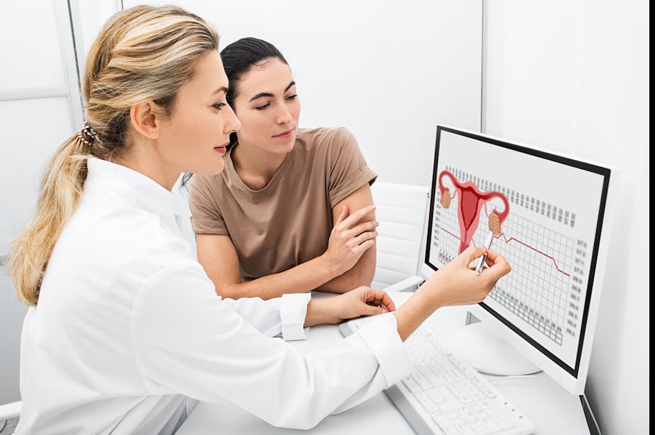 A female doctor and female patient look at a diagram of a uterus on the computer to understand the patient's fertility.
