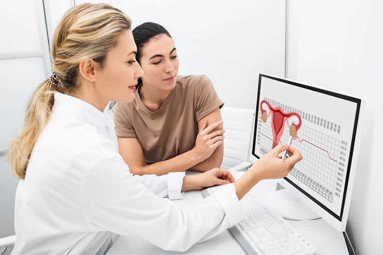 A female doctor and female patient look at a diagram of a uterus on the computer to understand the patient's fertility.