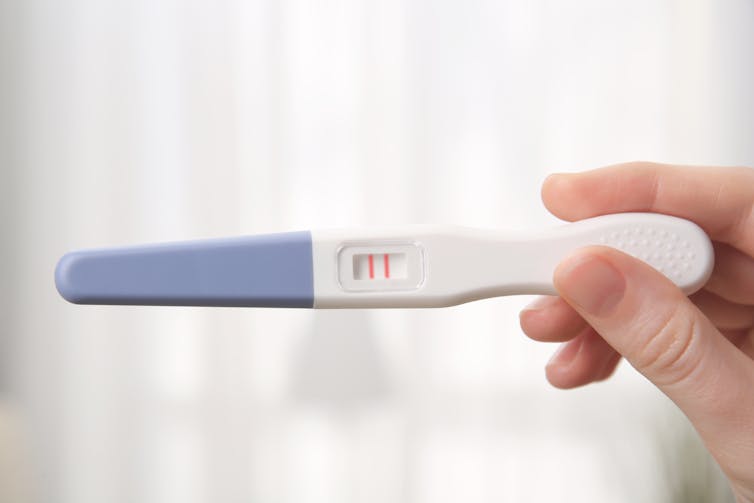 A woman holds a positive pregnancy test in her hand.