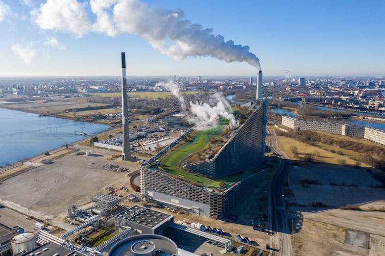 A large modern building with a grassy sloped roof and chimney billowing white smoke.