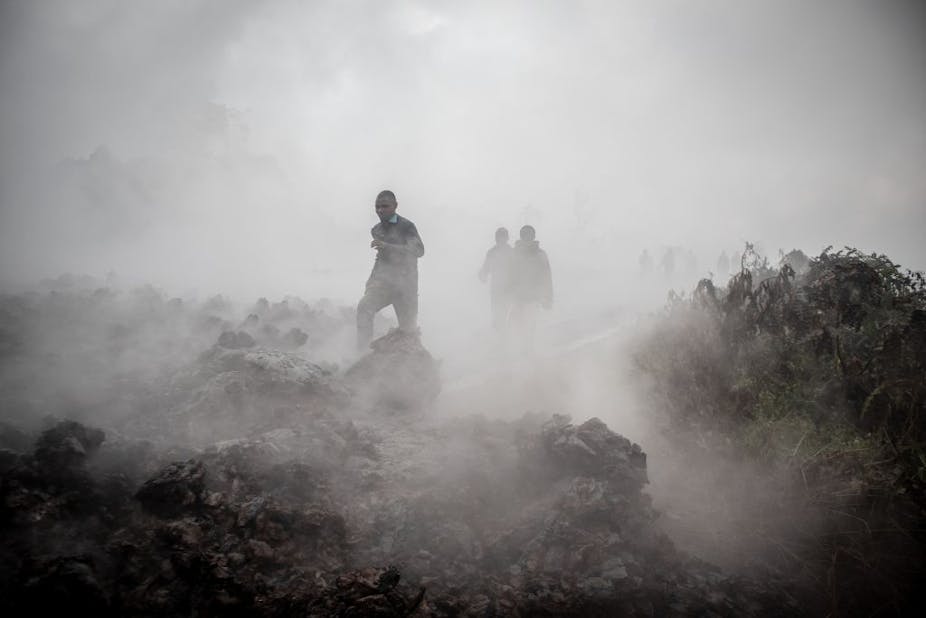 Men cross the front of the still smoking lava rocks from an eruption of the Mount Nyiragongo 