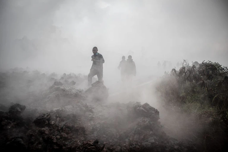 Men cross the front of the still smoking lava rocks from an eruption of the Mount Nyiragongo