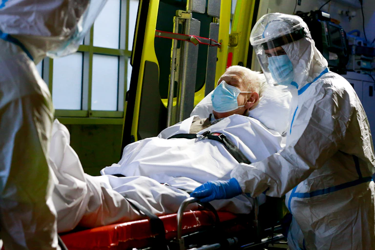 Medical staff in Belgium in PPE transferring a man from an ambulance to a hospital