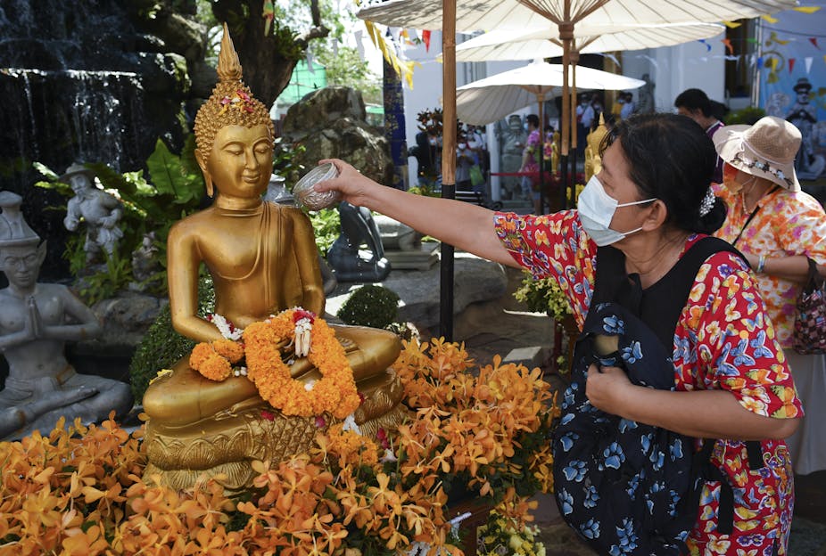 A woman pours scented water on a Buddha statue at Wat Pho temple in Bangkok, Thailand.