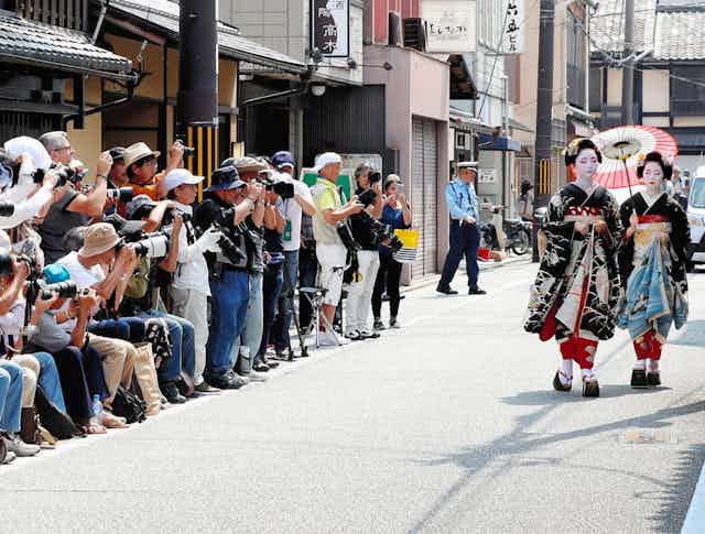 Des touristes agglutinés photographient deux geishas qui marchent sur la rue.
