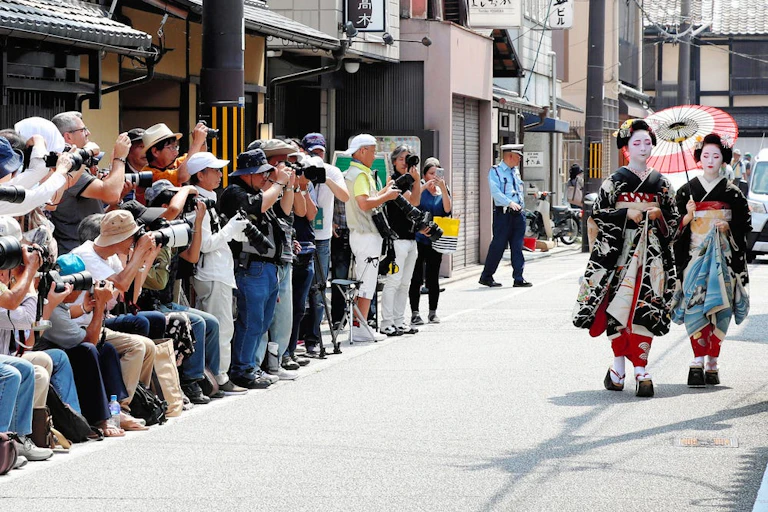 Des touristes agglutinés photographient deux geishas qui marchent sur la rue.