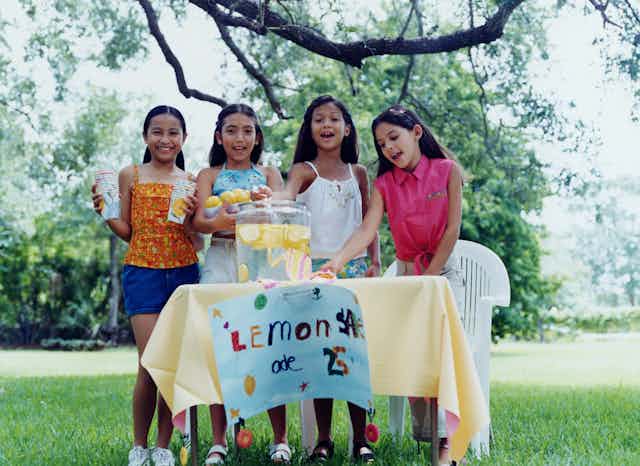 four young girls outside standing behind a table selling lemonade for 25 cents