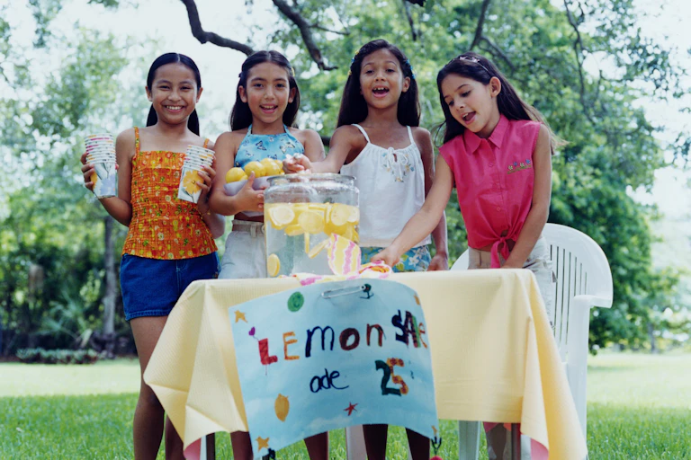 four young girls outside standing behind a table selling lemonade for 25 cents