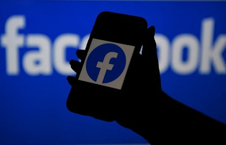 A silhouetted hand holding a phone with the Facebook logo on it