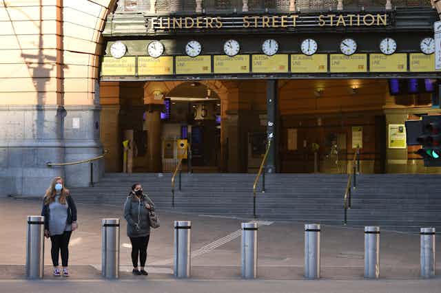 Two people wearing masks standing outside Flinders Street Station in Melbourne, Victoria
