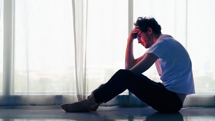 A man sitting on the floor at home appears unhappy.