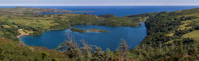 A large blue lake surrounded by green hills and the ocean beyond.