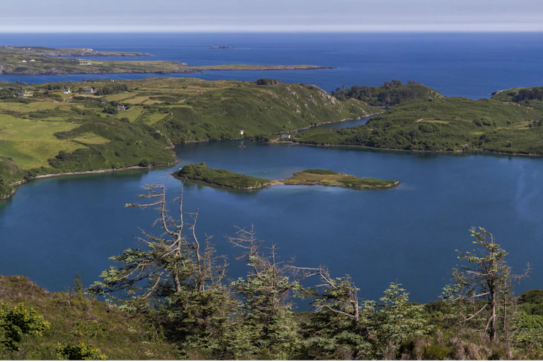 A large blue lake surrounded by green hills and the ocean beyond.