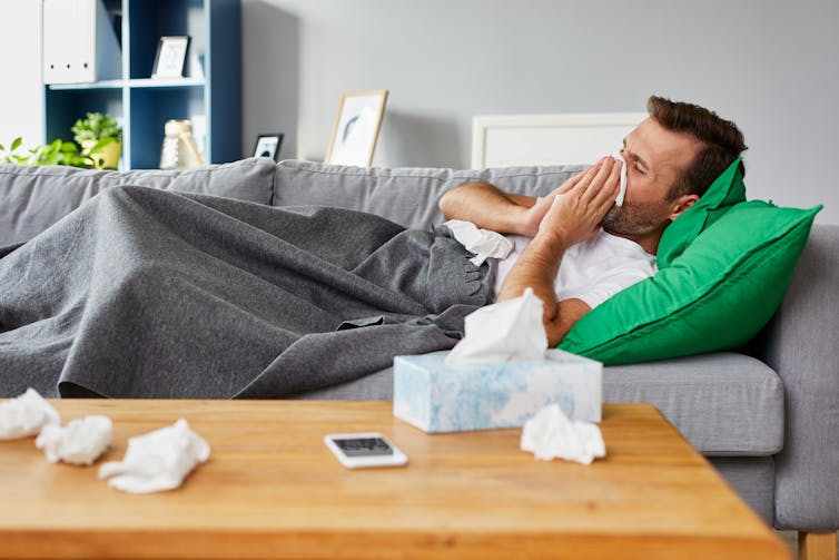 Sick man lying on the couch blows his nose with a tissue. Immune system and time of day