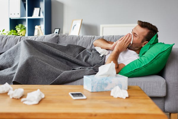 Sick man lying on the couch blows his nose with a tissue.