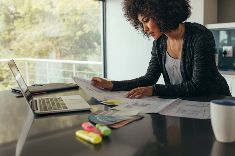 Young Black woman working at her kitchen top counter with computer and coffee.