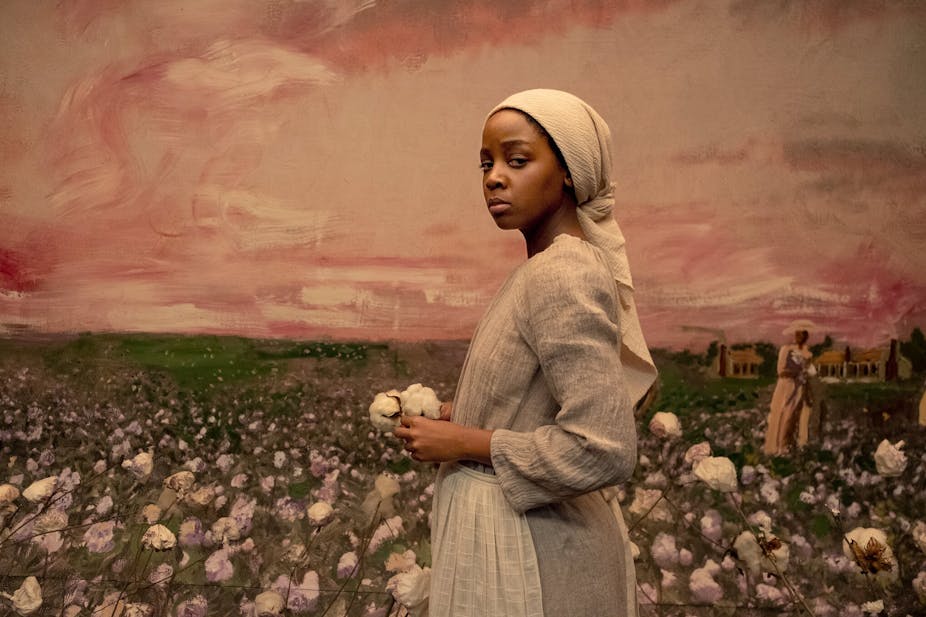 A woman holding cotton against a painting of a cotton field. 