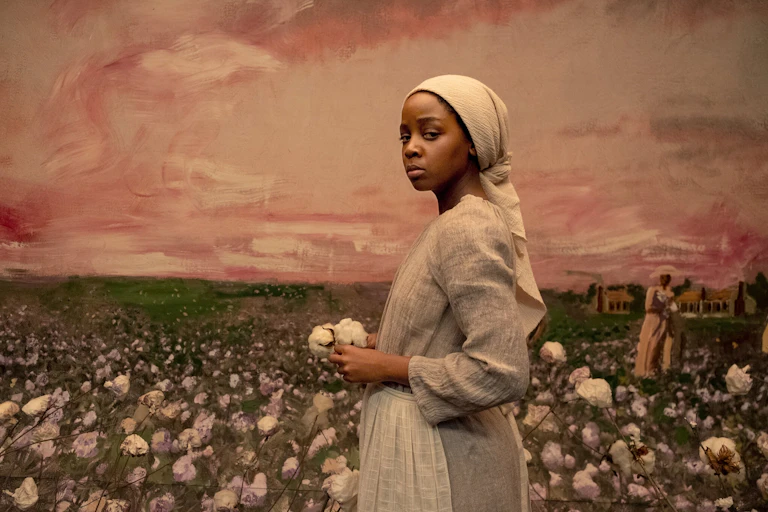 A woman holding cotton against a painting of a cotton field.
