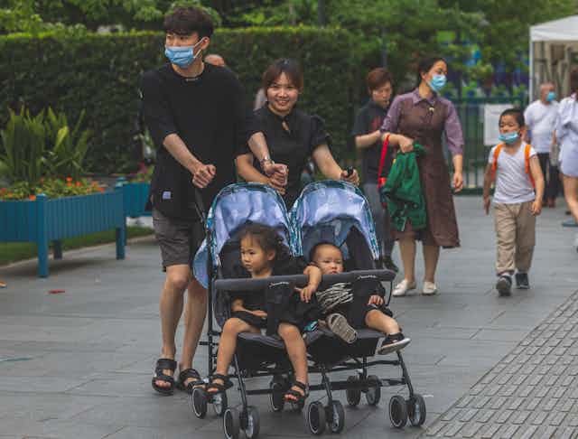 A couple in Shanghai pushes a double stroller with two small children in it.