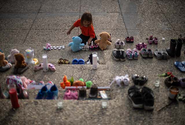 Une fillette allume des bougies, entourée de souliers d'enfants et de peluches