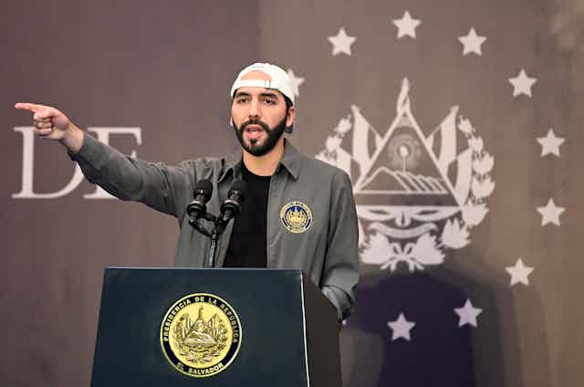 Bukele, wearing his signature backwards baseball cap, stands at a lectern and points 