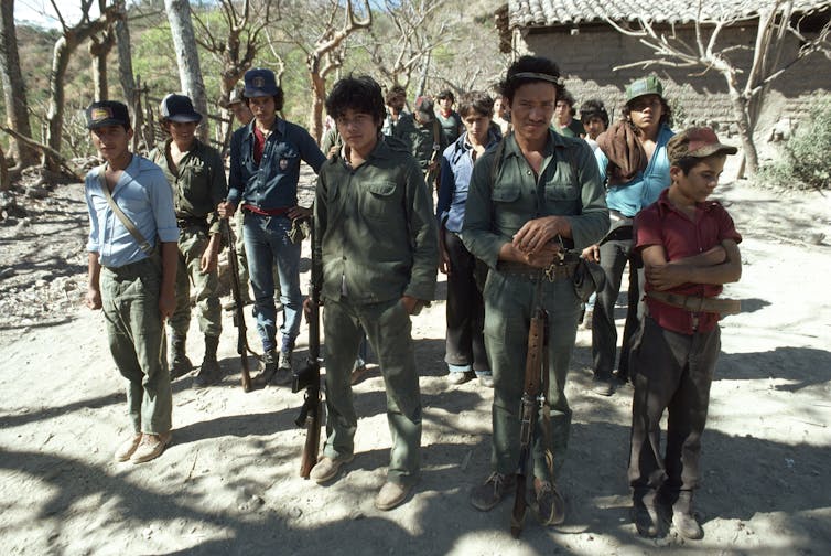 Young people, some in fatigues carrying weapons, stand in formation