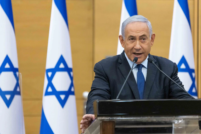 Benjamin Netanyahu speaks at a podium in front of four Israeli flags.