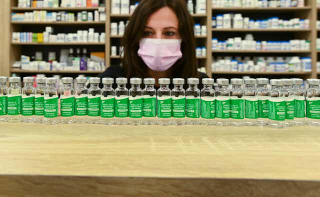 A woman in a face mask behind a long row of empty vaccine vials