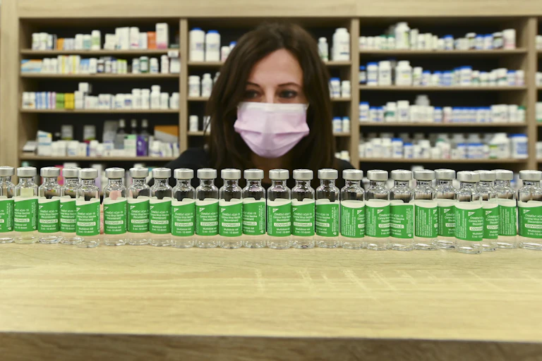 A woman in a face mask behind a long row of empty vaccine vials