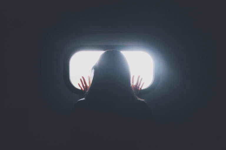 Woman stares looking out a small window in a dark room